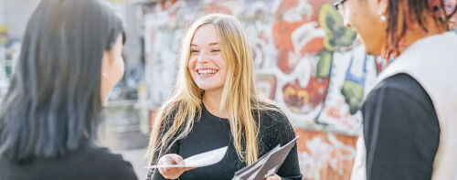 vrouw met lang blond haar deelt papier uit aan mensen